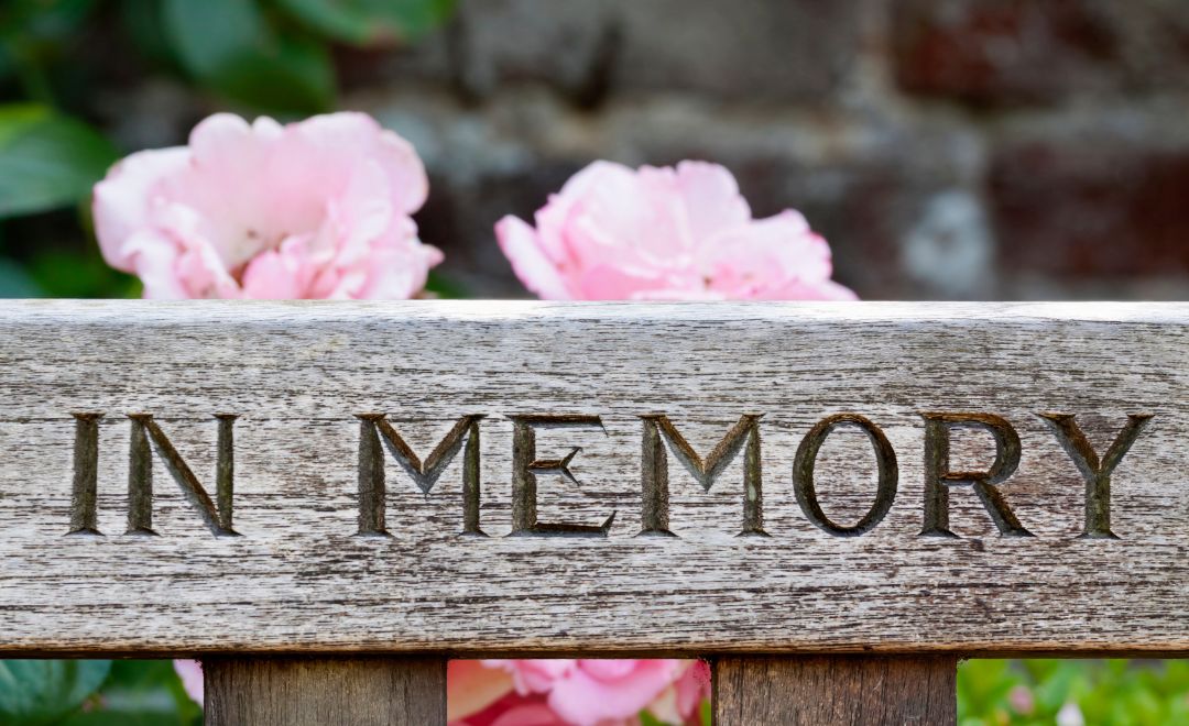 "In Memory" carved in wood in front of pink flowers