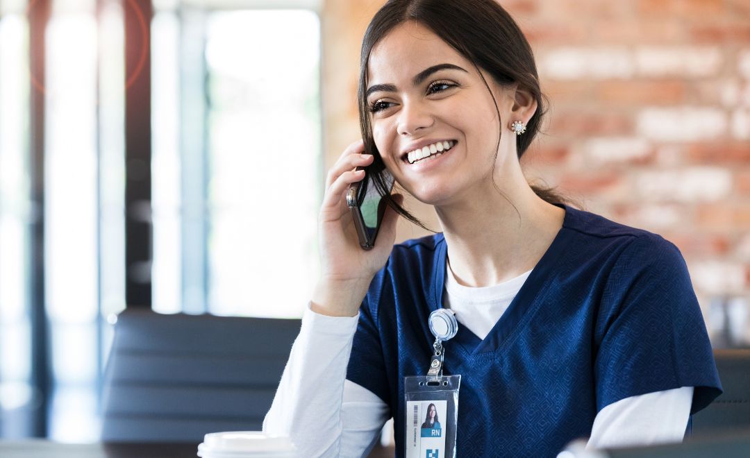 A smiling nurse in navy scrubs on the phone
