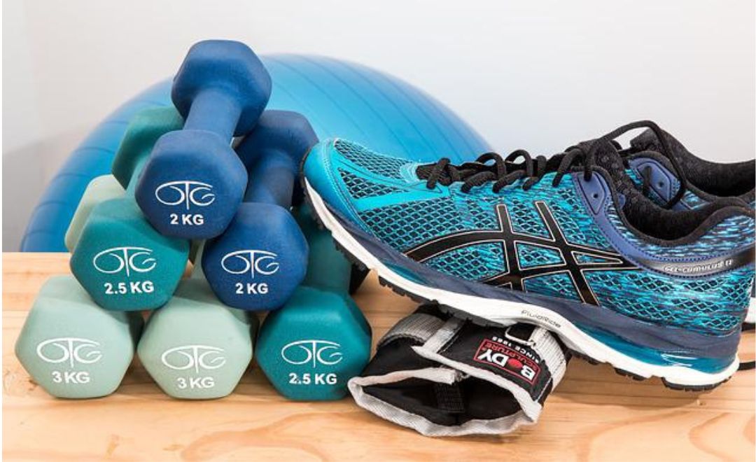 A running shoe next to a pile of hand weights with a pilates ball in the background