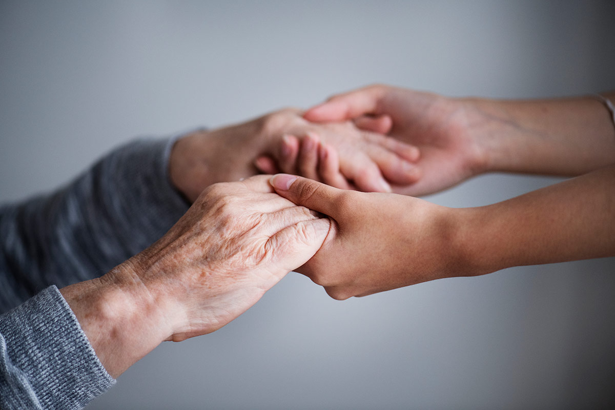 Close-up of a younger person's hands holding an older person's hands
