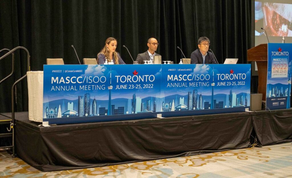 Three panelists sitting behind a panel at MASCC/ISOO 2022